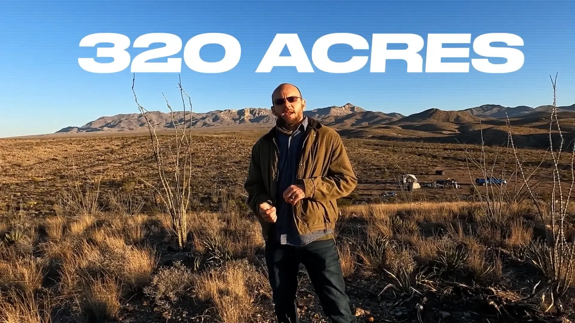 Sean Overton stands in a barren desert with a tent and a truck in the distance to introduce his desert land project. 